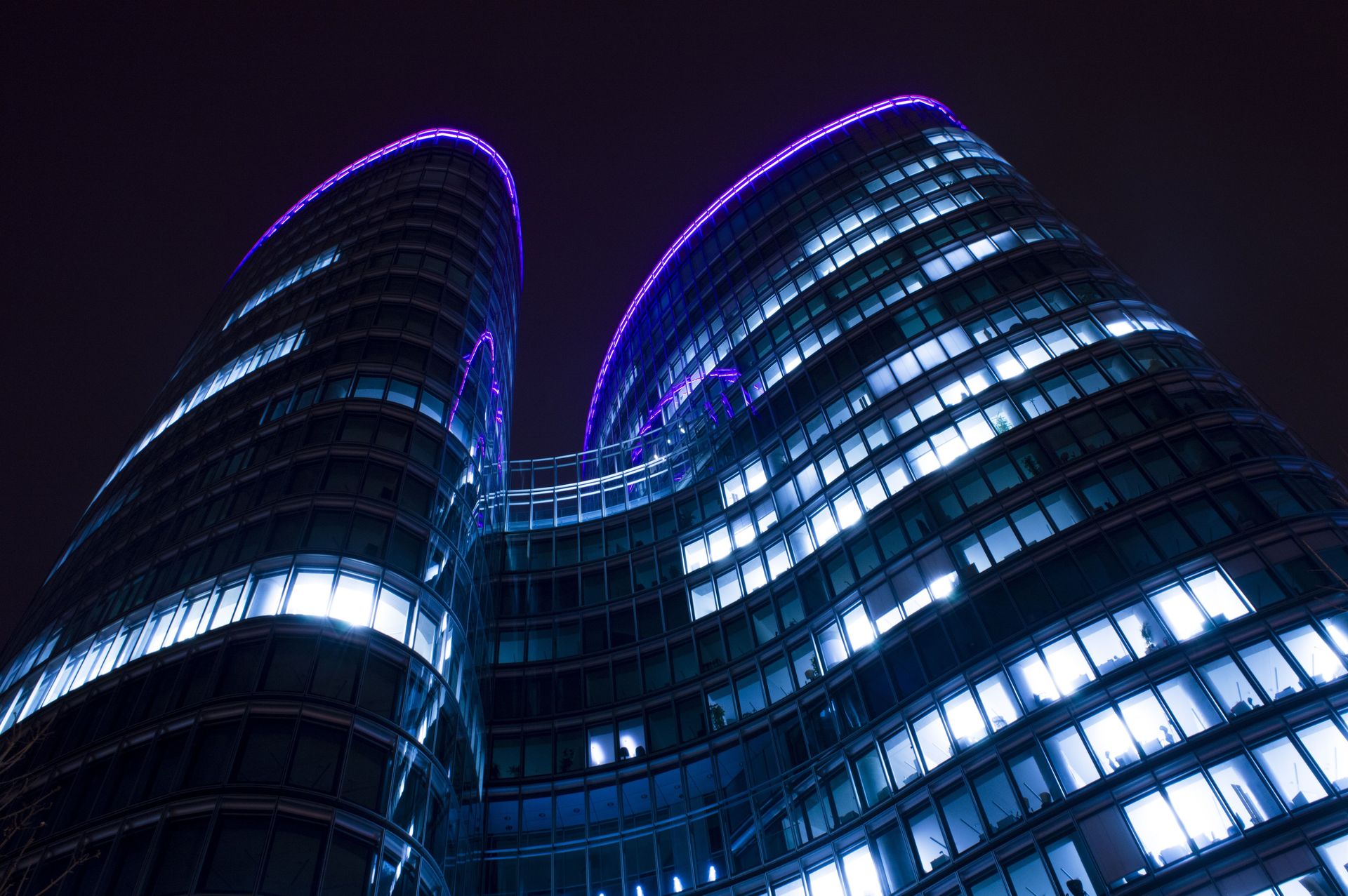 Low angle view of a modern skyscraper with glowing lights and purple accents against a night sky.